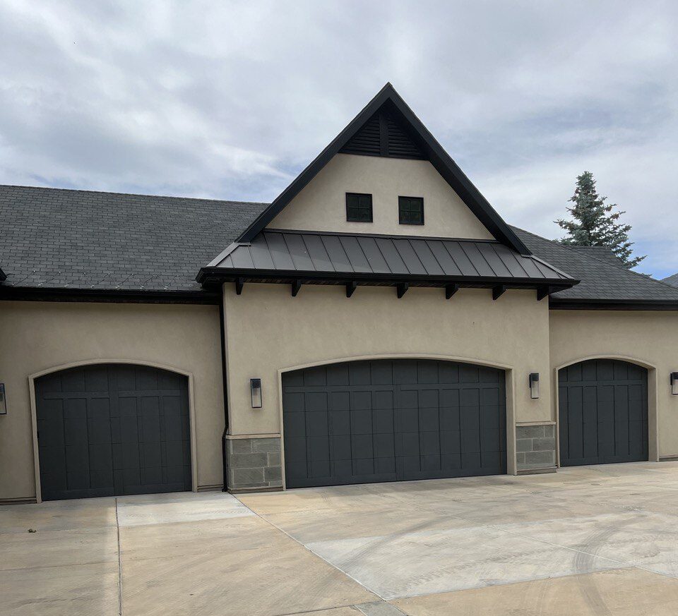 The exterior of a stucco home with three painted garage doors. The doors are brown and the stucco a sand tone tan.